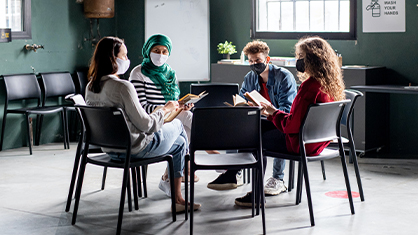 A group of four people sitting in a circle with mask on having a discussion