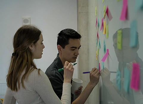 female and male students writing on sticky notes on the board