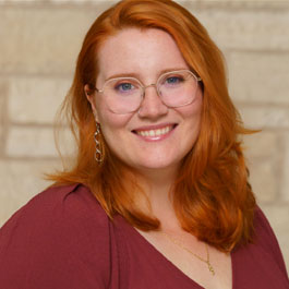 white woman with red hair and glasses wearing a sweater and smiling