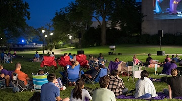 Students sit on a lawn at night watching a movie